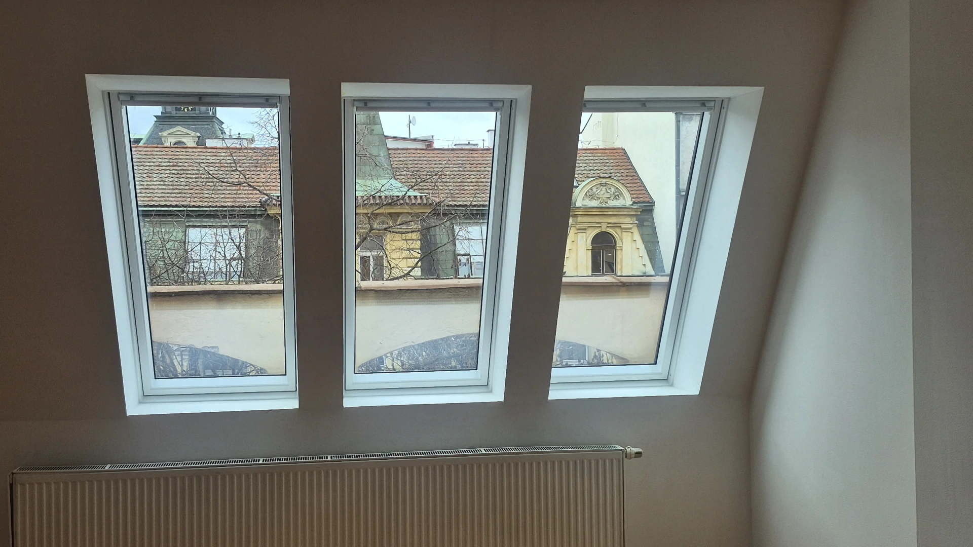 Trojice střešních oken VELUX po výměně s výhledem na historické střechy