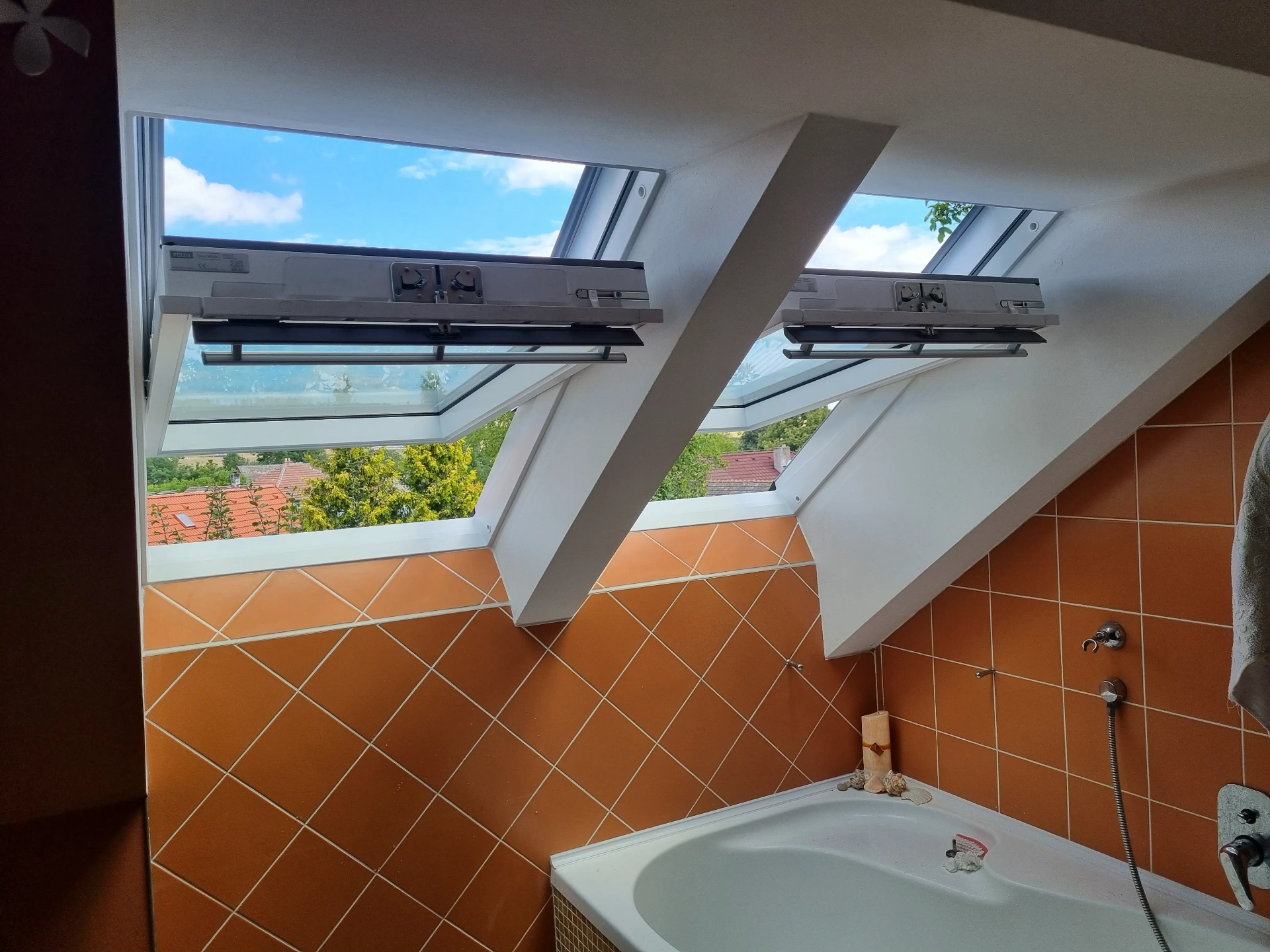 Dvojice otevřených střešních oken VELUX v koupelně s výhledem do krajiny