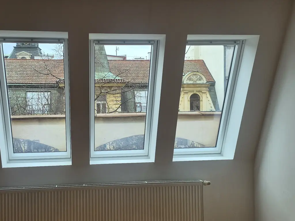 Trojice střešních oken VELUX po výměně s výhledem na historické střechy